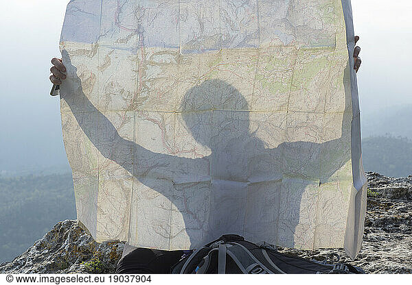 Detail of woman silhouetted in map on bluff above mountains