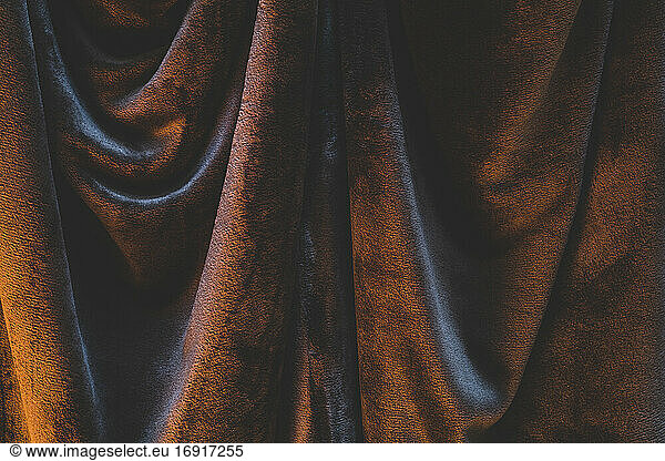 Detail von drapiertem und zerknittertem Samtstoff  stimmungsvolle warme Beleuchtung  die Falten und Knicke beleuchtet