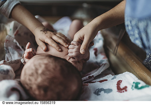 Detailansicht der Geschwister  die im Krankenhaus die Hand des neugeborenen Bruders halten