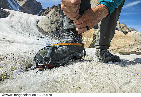 Detailansicht eines Bergsteigers  der seine Steigeisen vor dem Aufstieg anzieht.