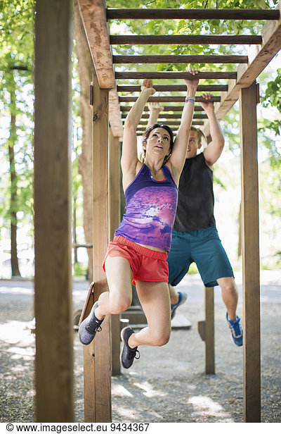 Determined couple hanging on monkey bars at outdoor gym