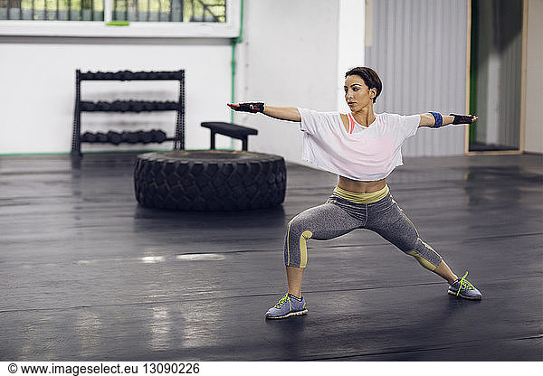 Determined female athlete exercising in Warrior 2 pose at gym