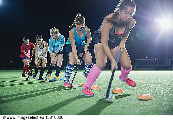 Determined female field hockey players practicing sports drill on field at night