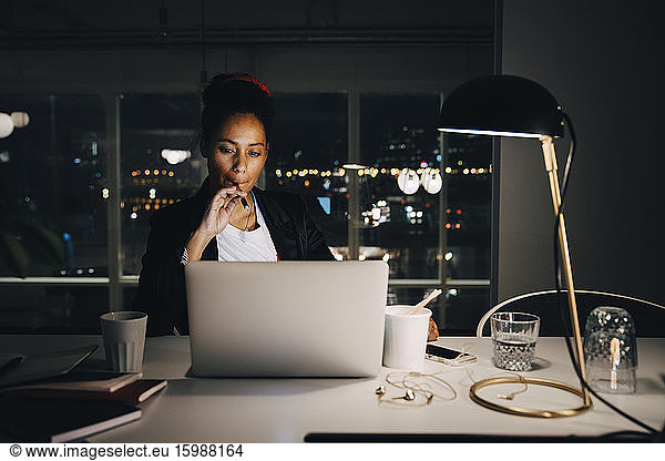 Determined female professional looking at laptop while sitting and working late in coworking space