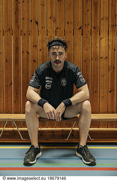 Determined male athlete sitting on bench at sports court