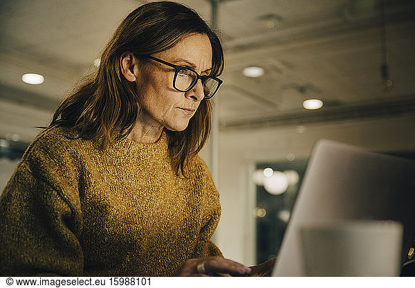 Determined mature female entrepreneur working late while using laptop at workplace