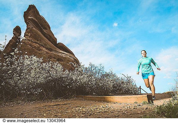 Determined sportswoman jogging on dirt trail by rock formation against sky