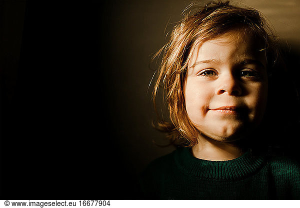 Determined toddler girl standing in bright light smiling