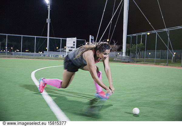 Determined young female field hockey player running for the ball  playing on field at night