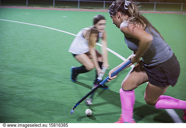 Determined young female field hockey players reaching for the ball with hockey sticks  playing on field