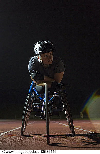 Determined young female paraplegic athlete training for wheelchair race on sports track at night