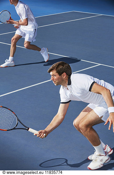 Determined young male tennis doubles players poised with tennis rackets on tennis court