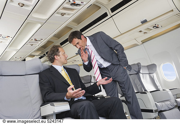 Deutschland  Bayern  München  Geschäftsleute flüstern in Business Class Flugzeugkabine