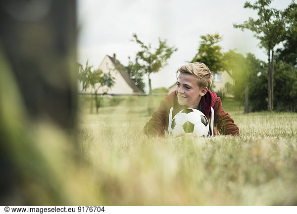 Deutschland  Mannheim  Teenage boy wizh soccer ball  liegend auf Gras