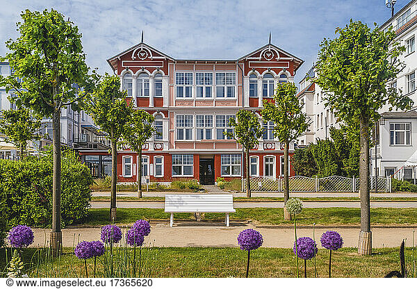 Deutschland  Mecklenburg-Vorpommern  Heringsdorf  Blühende Blumen vor einer leeren Parkbank mit Hotel im Hintergrund