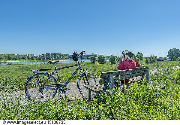 Deutschland  Zons  älterer Mann mit Fahrrad  der sich auf einer Bank ausruht und die Aussicht betrachtet