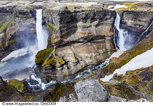 Die atemberaubenden erdigen Farben und Felsformationen zusammen mit dem ungeschmolzenen Schnee  der in der Talsohle des Haifoss zwischen zwei Wasserfällen ruht. Natürliche Schönheit an einem der großartigsten Aussichtspunkte für Wanderungen in Island  Island