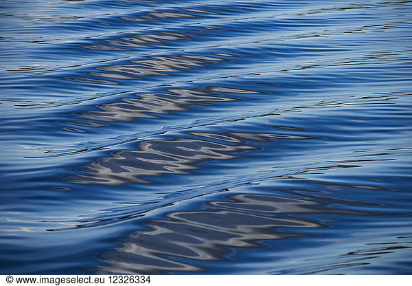 Die blauen  schwarzen und weißen Reflexionen des Himmels  der Wolken und des nahegelegenen Landes im Kielwasser eines Bootes im Puget Sound  Washington  erzeugen eine schöne Textur und ein Gefühl der Bewegung; Puget Sound  Washington  Vereinigte Staaten von Amerika