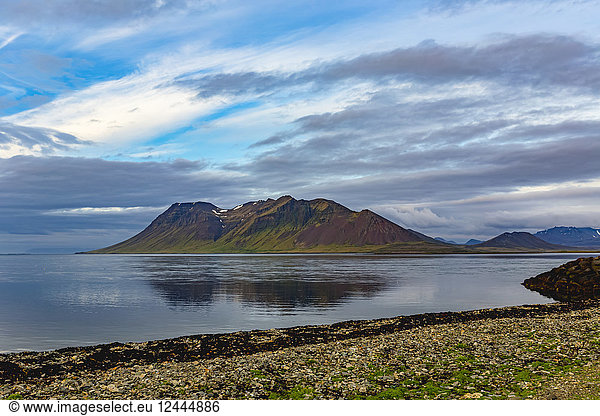 Die farbenfrohen vulkanischen Hügel spiegeln sich bei Sonnenuntergang im Westen Islands auf dem Meer.