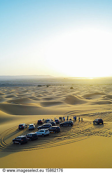 Die Menschen beobachten den Sonnenuntergang in der marokkanischen Wüste von ihren 4x4-Autos aus