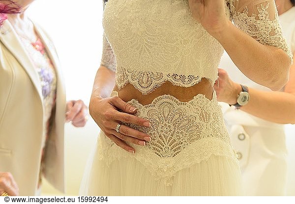 Die Mutter der Braut hilft der Tochter am Hochzeitstag beim Anziehen des Brautkleides