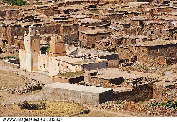 Die Ortschaft Ait Ourhaine mit islamischer Moschee und Minarett  im Vordergrund treibt ein Mann Esel über einen Dreschplatz um Stroh zu häckseln  Antiatlas  Südmarokko  Marokko  Afrika