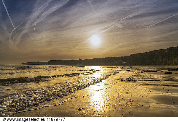 Die untergehende Sonne leuchtet am Himmel und spiegelt sich auf dem nassen Sand entlang der Küste; South Shields  Tyne and Wear  England