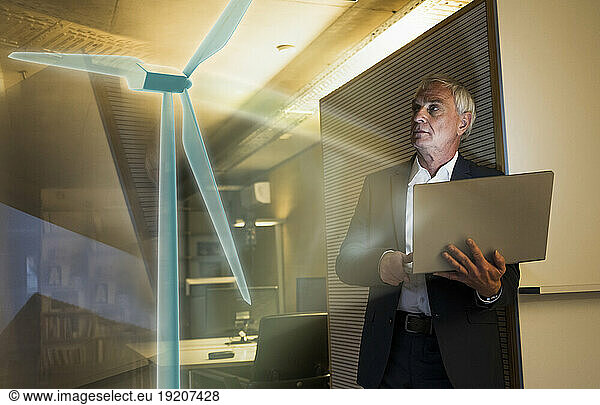 Digital composite image of businessman looking at futuristic wind turbine in office