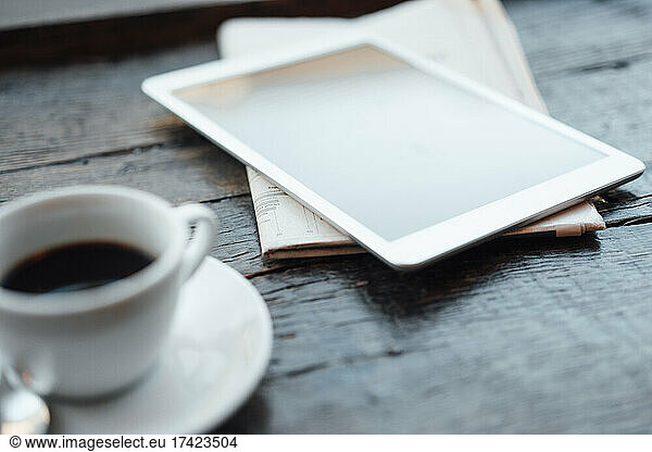 Digital tablet with coffee cup and newspaper on table in cafe