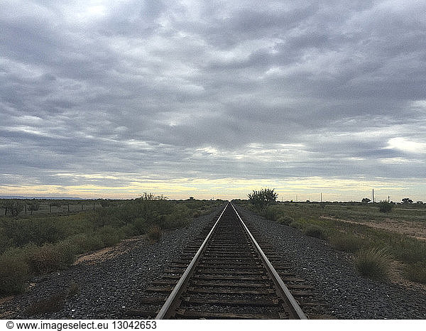 Diminishing perspective of railroad track against cloudy sky during sunset