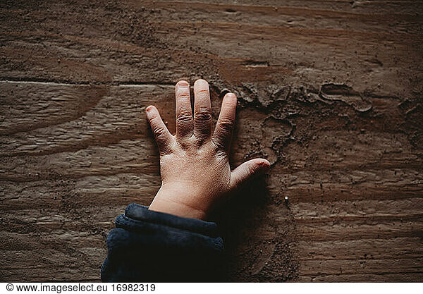 Dimpled baby hands on wooden board full of sand
