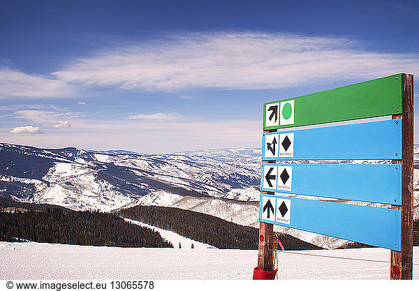 Directional sign board on snow covered mountain against sky