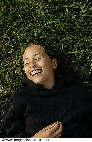 Directly above shot of carefree girl laughing while lying down on grass at summer camp