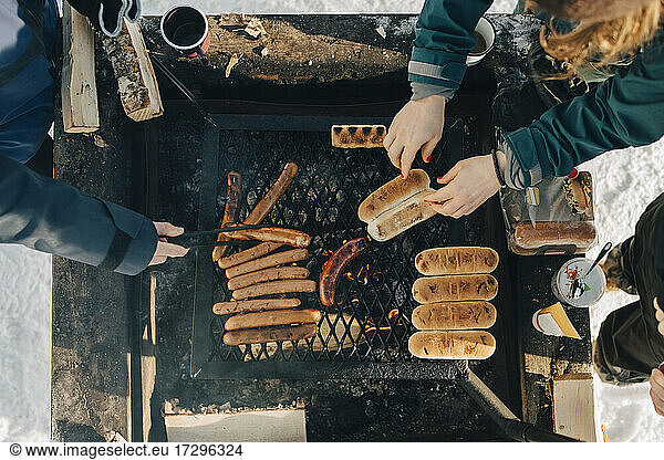 Directly above shot of friends preparing sausages on barbecue grill