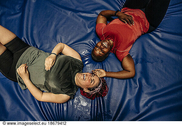 Directly above shot of happy female athletes lying on safety mat at sports court