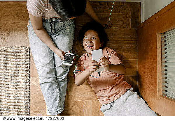 Directly above shot of happy siblings using smart phones on hardwood floor at home