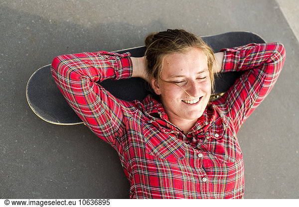 Directly above shot of happy woman lying her head on skateboard at skate park