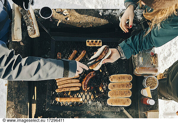Directly above shot of man serving sausage to female friend while cooking on barbecue grill