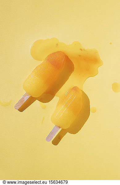 Directly above shot of melting popsicles on yellow background