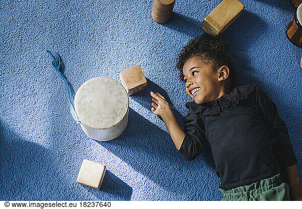 Directly above shot of smiling girl looking at wooden toy block at kindergarten