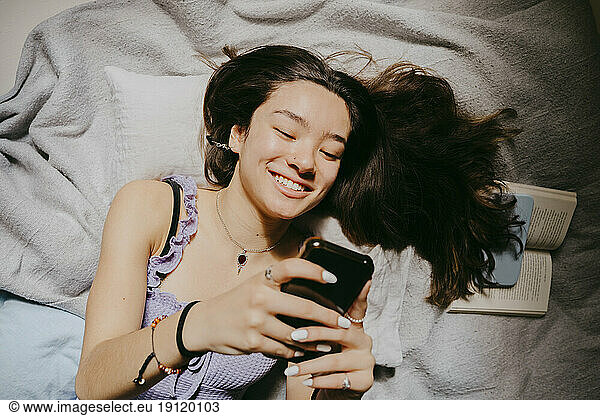 Directly above shot of smiling young woman using smart phone while lying on bed at home