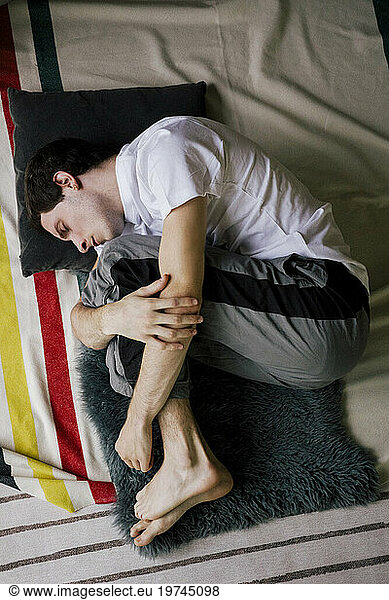 Directly above view of sad man lying down in fetal position on carpet at home