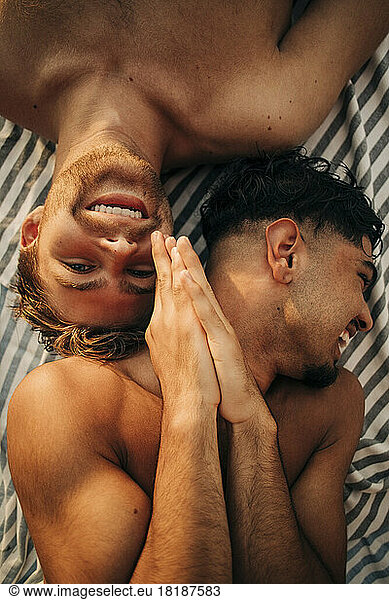 Directly above view of shirtless man with hands clasped lying down by male friend