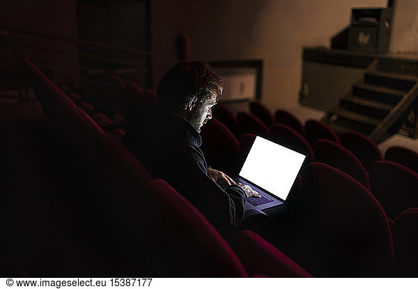 Director sitting at auditorium of theatre working on laptop