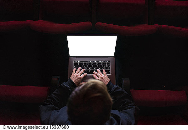 Director sitting at auditorium of theatre working on laptop  top view