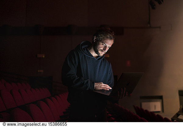 Director standing at auditorium of theatre using laptop