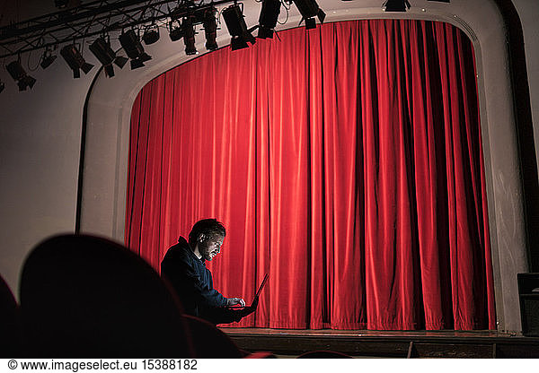 Director standing at auditorium of theatre using laptop