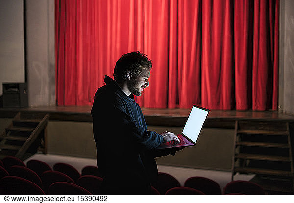 Director standing at auditorium of theatre using laptop