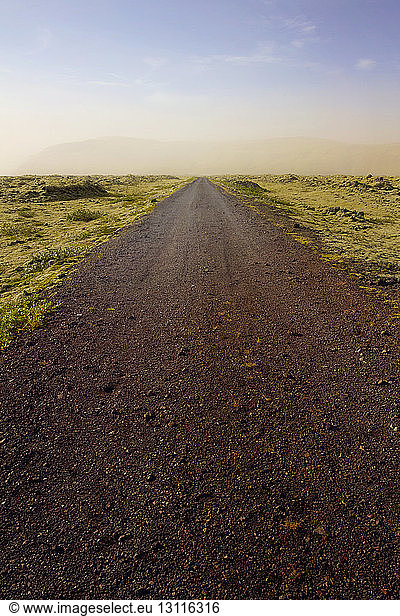 Dirt road on mossy landscape against sky