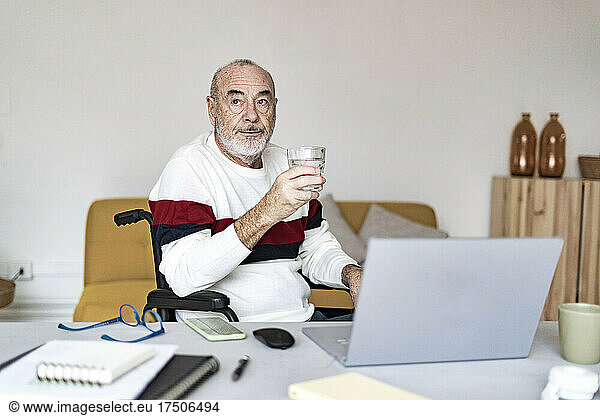 Disabled businessman holding drinking glass at home